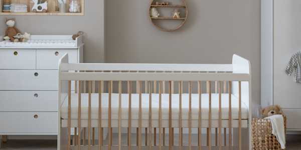A nursery with white and natural finish cot, chest, and wardrobe.
